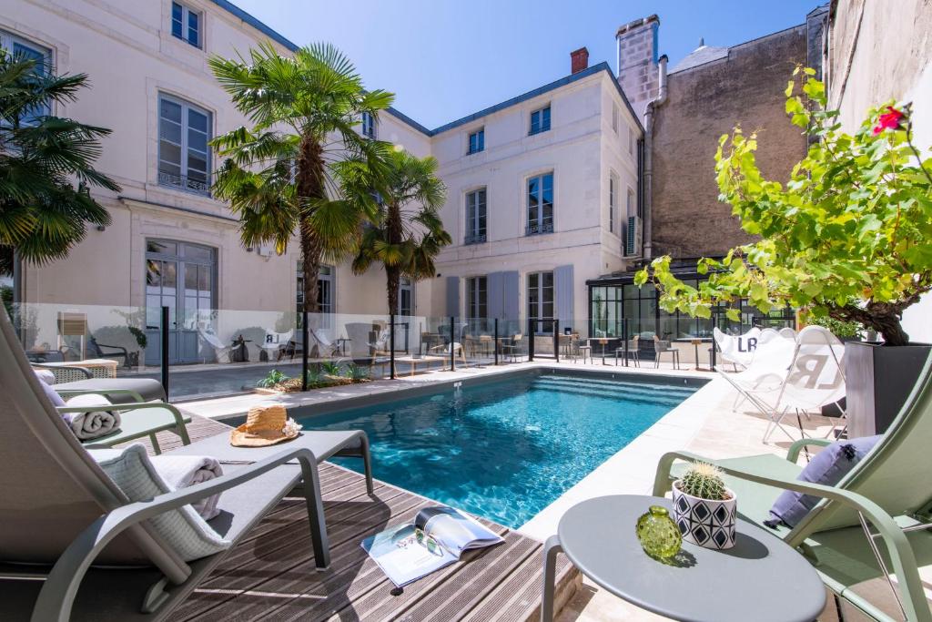 une piscine extérieure avec des chaises et un bâtiment dans l'établissement Villa Grand Voile - Christopher Coutanceau, à La Rochelle