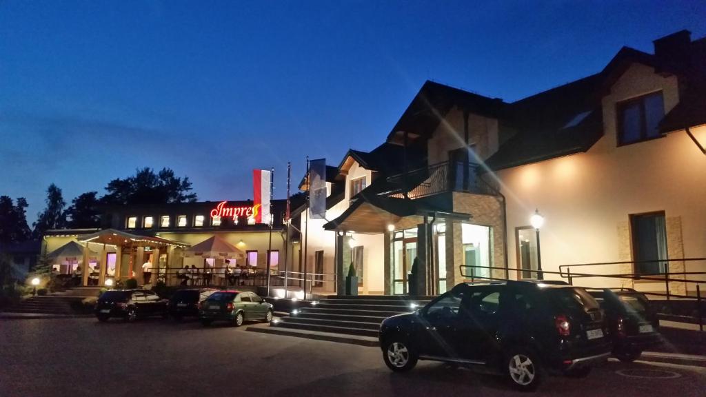 un edificio con coches estacionados en un estacionamiento por la noche en Hotel Impressa en Niedrzwica Duża