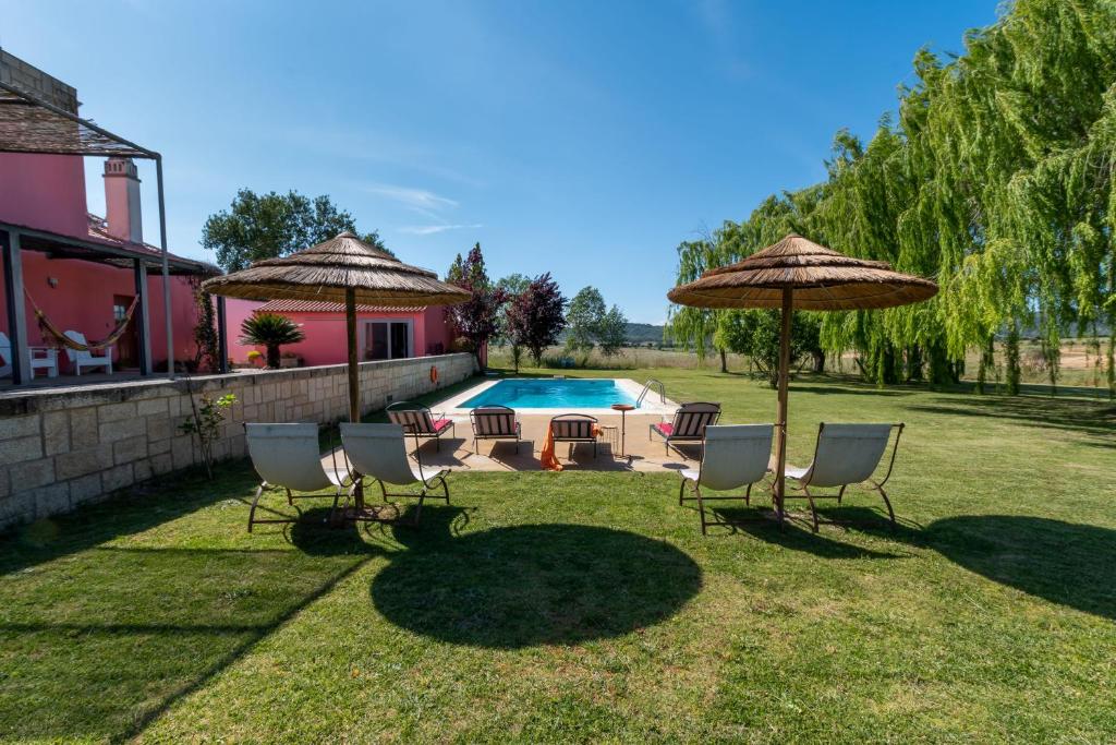 a group of chairs and umbrellas next to a pool at Casa das Jardas in Idanha-a-Nova