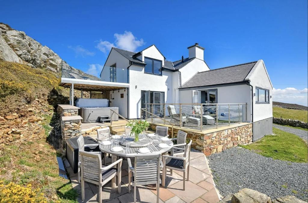 a white house with a table and chairs on a patio at Goferydd, South Stack, Anglesey, 4 bed luxury home, hot tub, dog friendly in Holyhead