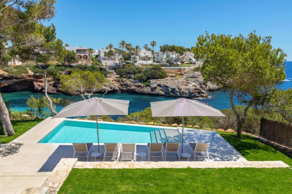 a swimming pool with chairs and umbrellas next to the water at Vista DOr in Cala d´Or