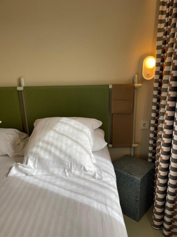 a bed with a green headboard and white pillows at Hotel des Victoires - Restaurant in Cannes