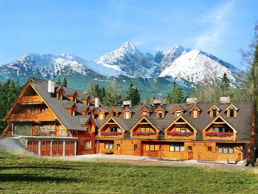 a large wooden house with mountains in the background at Penzión Teniscentrum in Tatranská Lomnica