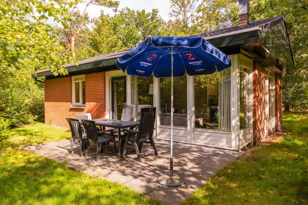 a table with chairs and an umbrella in front of a house at Summio Parc Heihaas in Putten