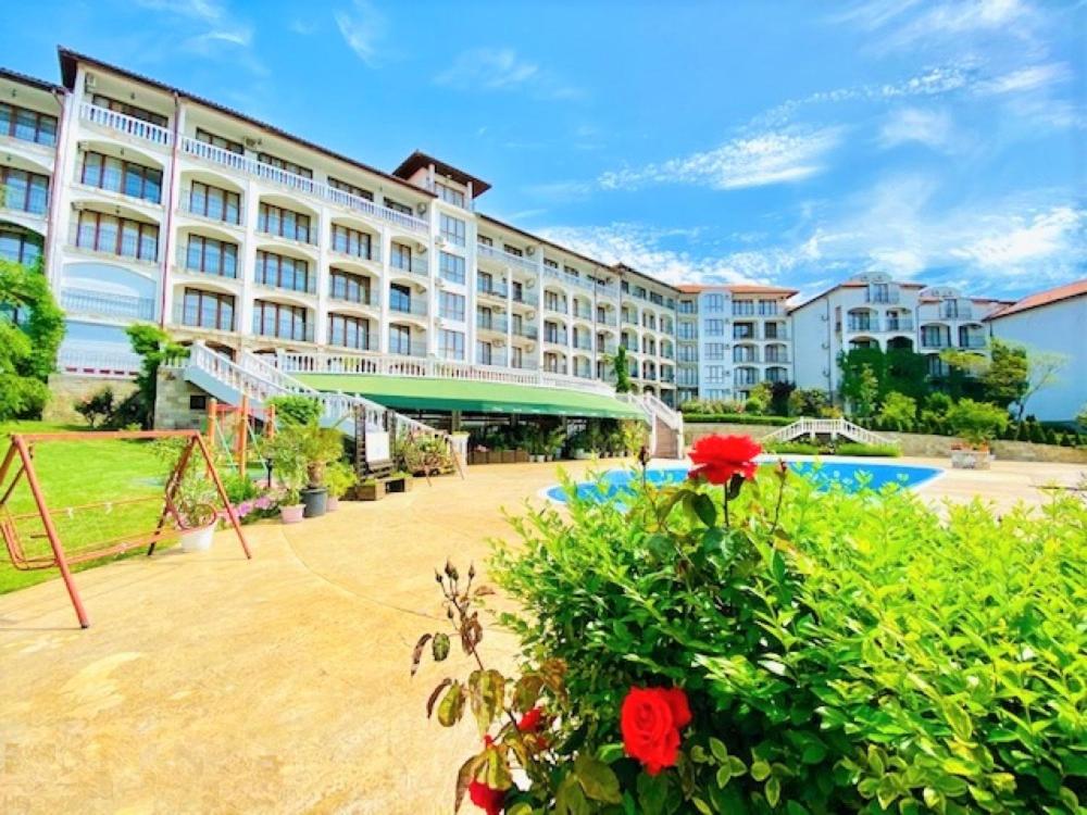 a large hotel with a courtyard with flowers in front of it at Студио Костови Имоти in Sveti Vlas