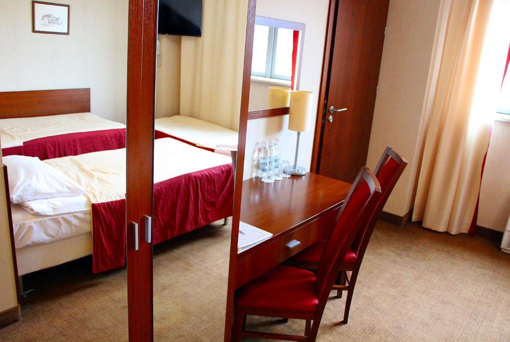 Twin hotel room with red bed runners, wooden desk and mirror, simple cozy decor