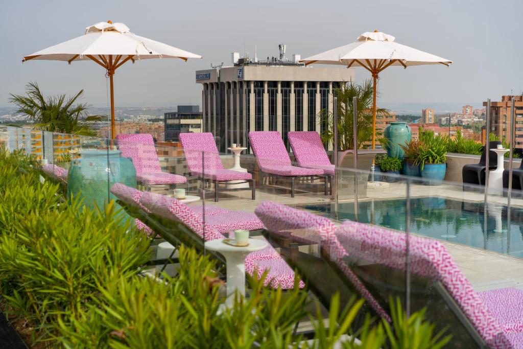 einen Balkon mit rosa Stühlen und einem Pool in der Unterkunft Hotel Pinar Plaza in Madrid