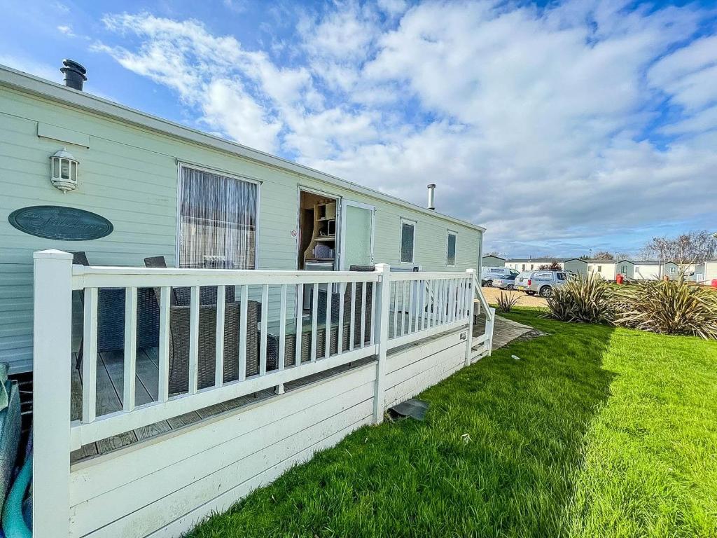 a house with a white fence next to a yard at Brilliant Caravan With Decking And Wifi At Dovercourt Park In Essex Ref 44010a in Great Oakley