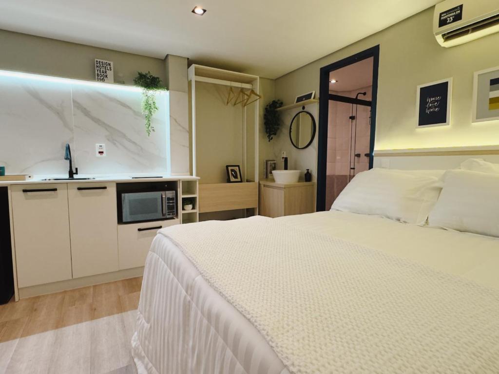 a bedroom with a white bed and a kitchen at Apê Paulista Alameda Santos in São Paulo