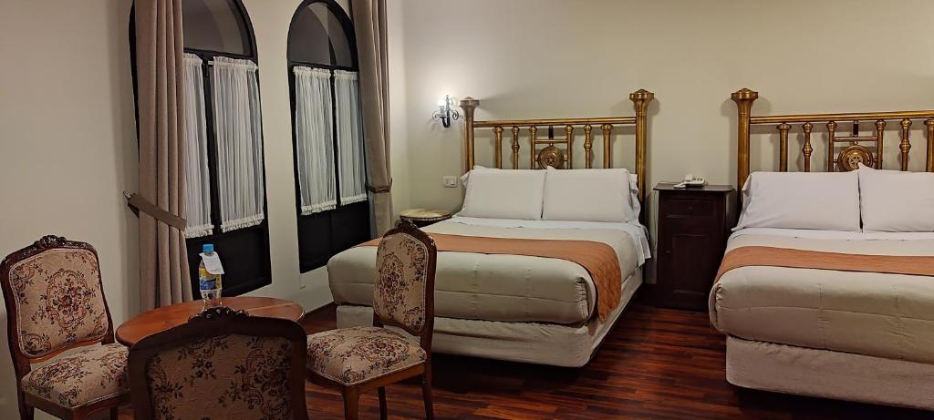 a bedroom with two beds and two chairs and a table at Hostal Colonial Potosi in Potosí