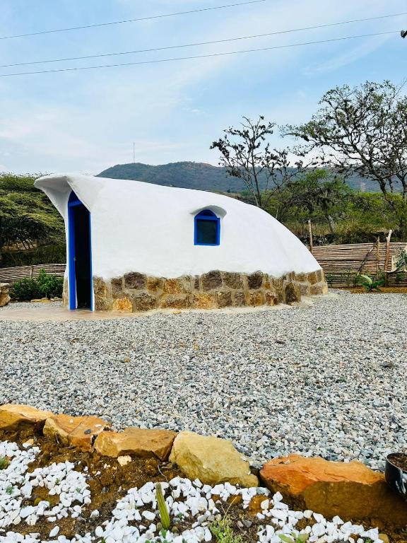 a large white building with blue windows on a gravel field at Bahareque glamping in Barichara