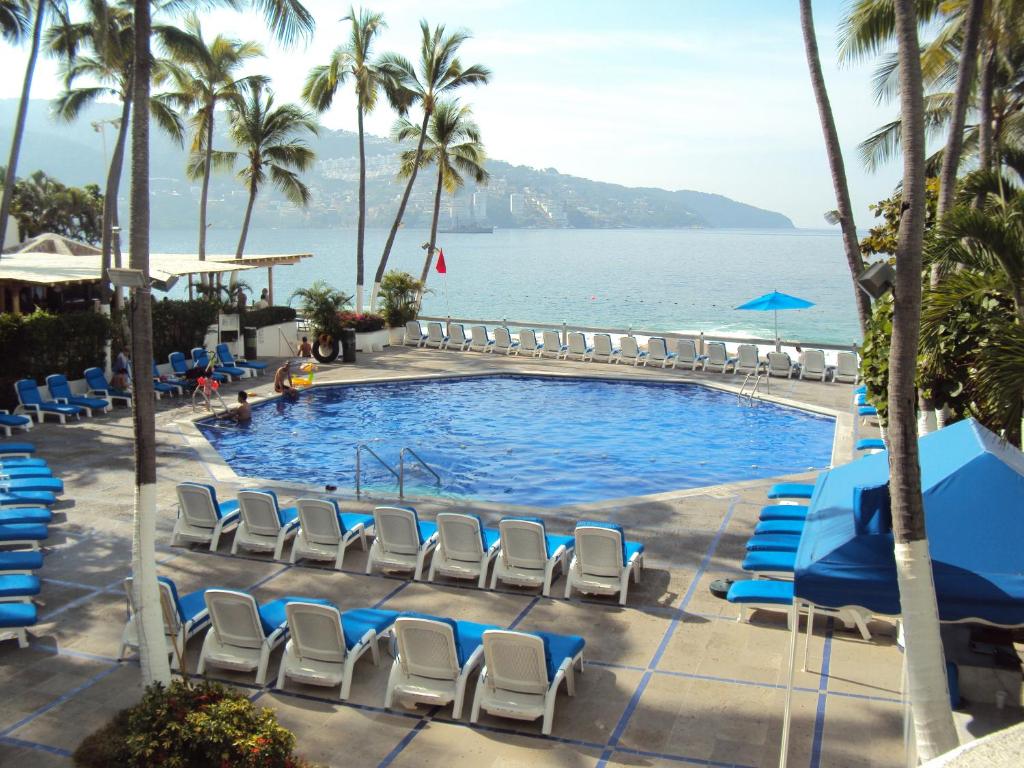 a pool with chairs and the ocean in the background at Hotel Acapulco Malibu in Acapulco