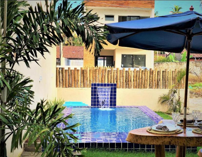 a swimming pool with an umbrella next to a house at Casa Conchas do Patacho in Pôrto de Pedras