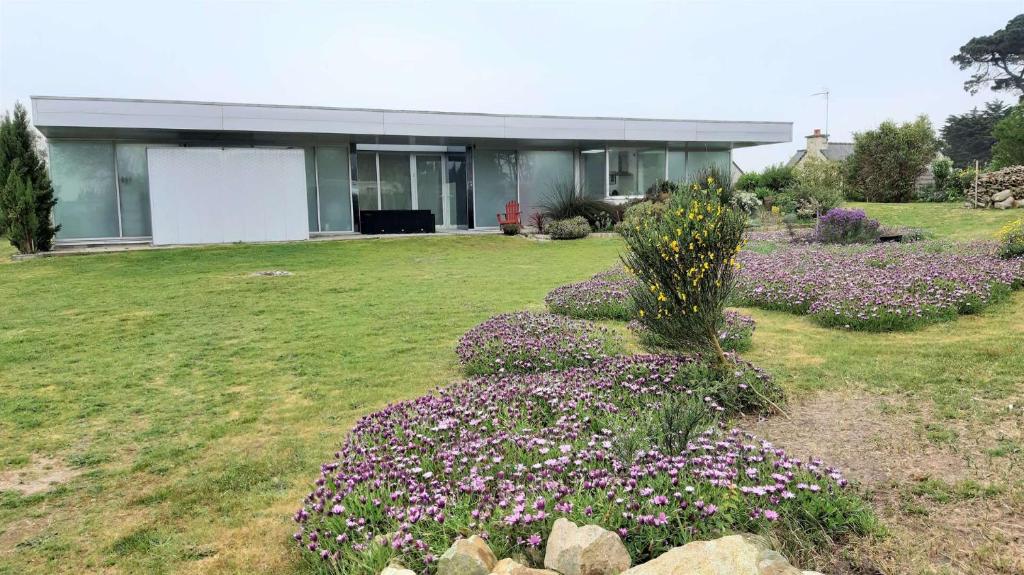 une maison avec des fleurs violettes devant une cour dans l'établissement Villa avec jardin à 370m de la plage de Landrellec à PLEUMEUR-BODOU REF-245, à Pleumeur-Bodou
