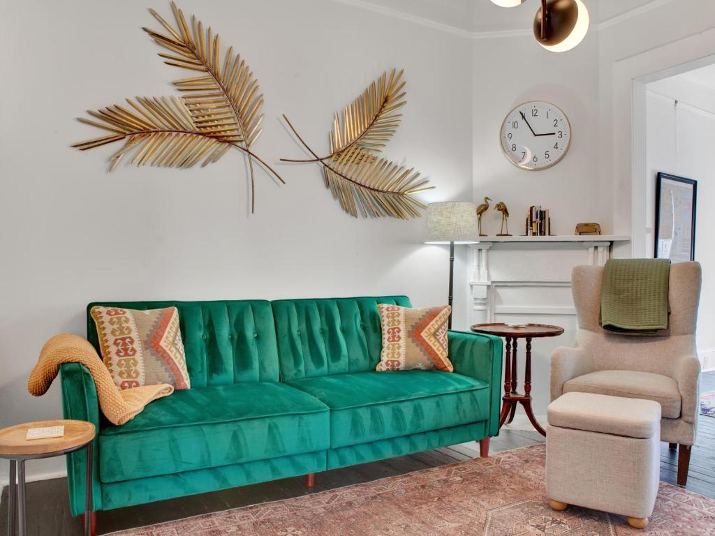 eine grüne Couch in einem Wohnzimmer mit Stuhl und Uhr in der Unterkunft Hiatus House in Savannah