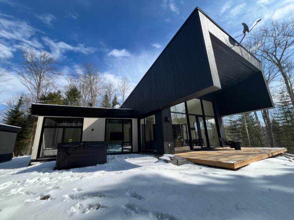 una casa con techo negro en la nieve en Au Haut De La Colline Spa Et Sauna, en St-Etienne de Bolton