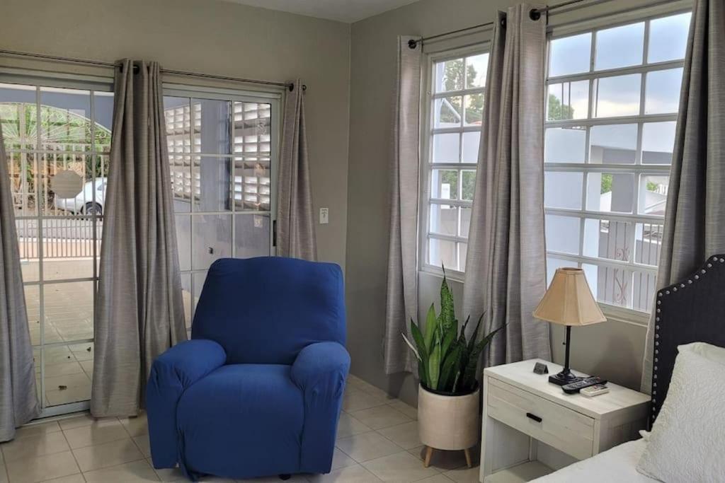 una silla azul en un dormitorio con ventanas en Coamo Beautiful house, AC, 10min Coamo hot springs, en Coamo