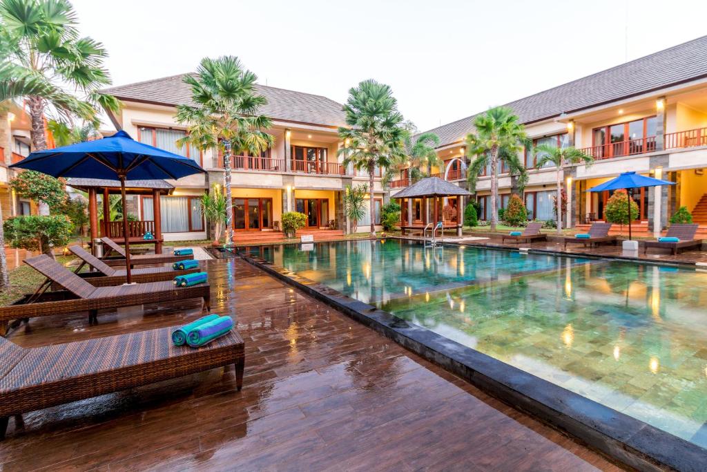 a swimming pool with benches and umbrellas in front of a building at Vidi Boutique Hotel in Nusa Dua