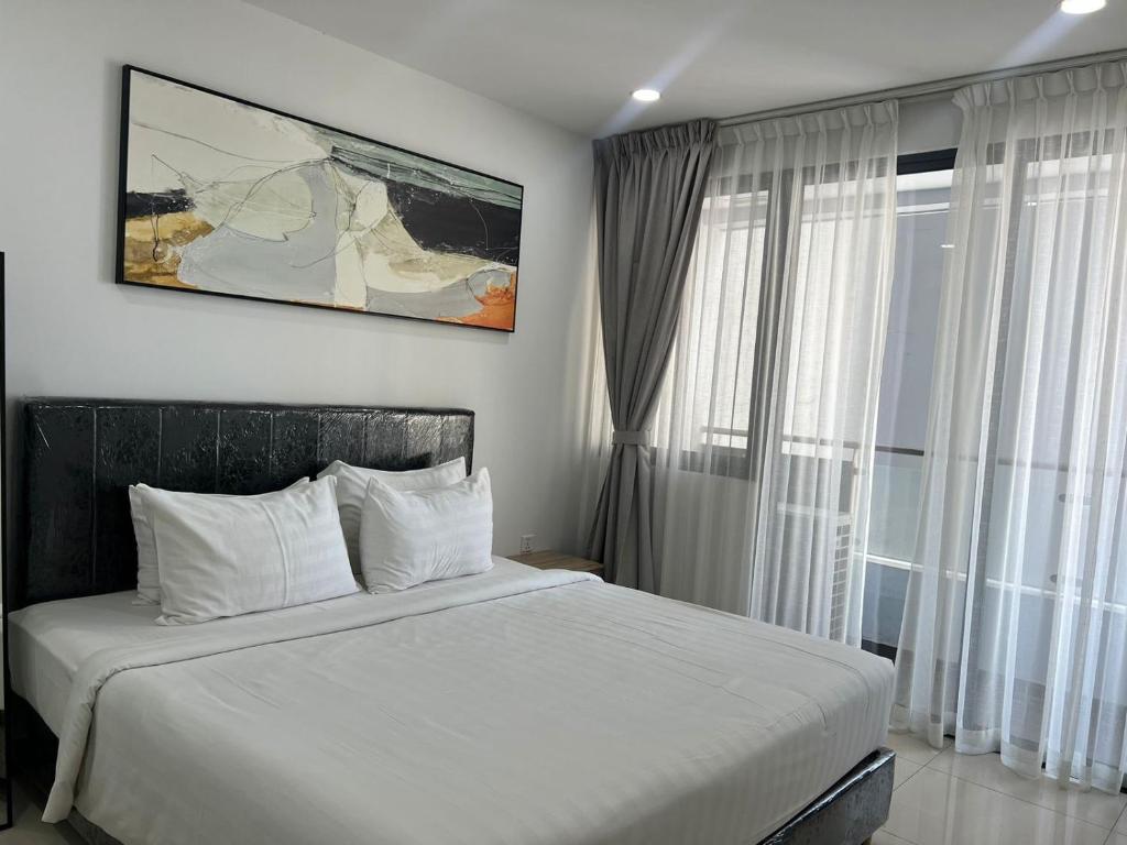 Cette chambre comprend un lit avec des draps blancs et une grande fenêtre. dans l'établissement De-Luxe Residence, à Phnom Penh