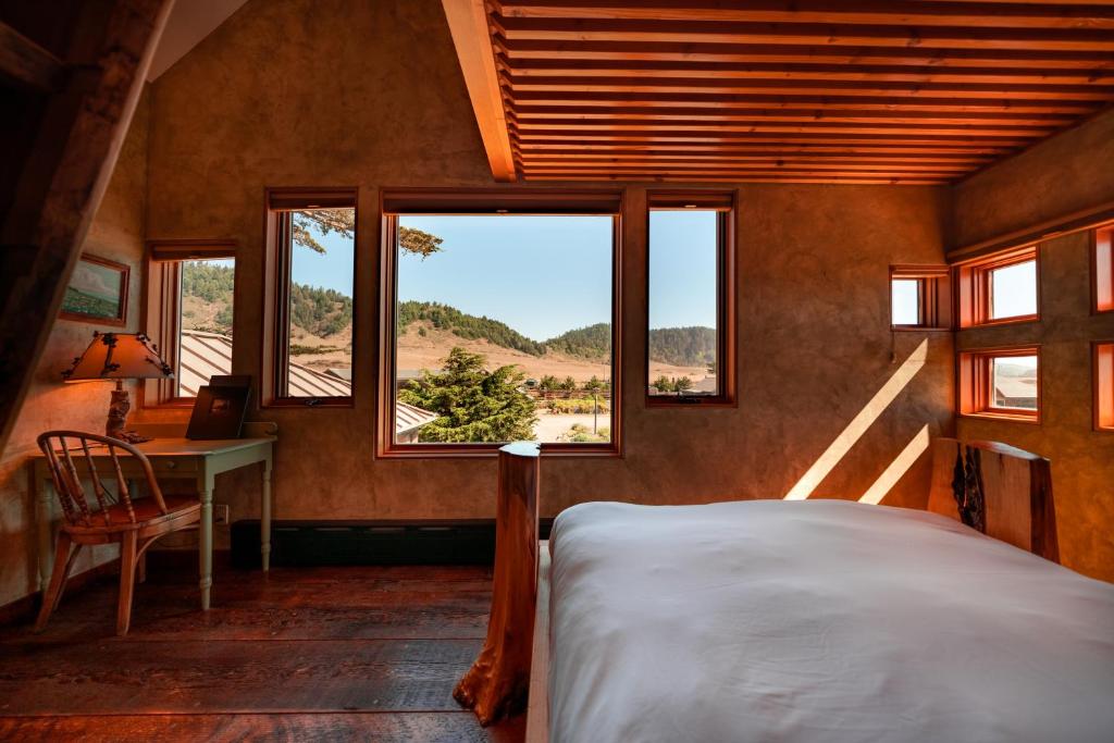 a bedroom with a bed and a desk and windows at The Inn at Newport Ranch in Fort Bragg