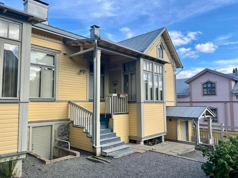 a yellow house with a porch and stairs at 19th century house with parking hall, own entrance and terrace in Vaasa