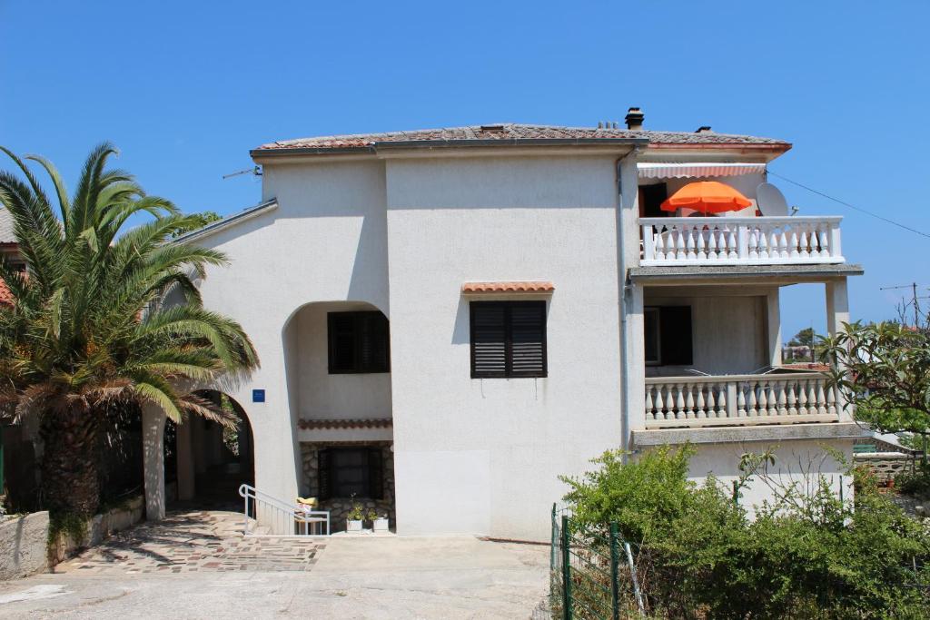 a white house with a balcony with an orange umbrella at Apartment Muzic in Mali Lošinj