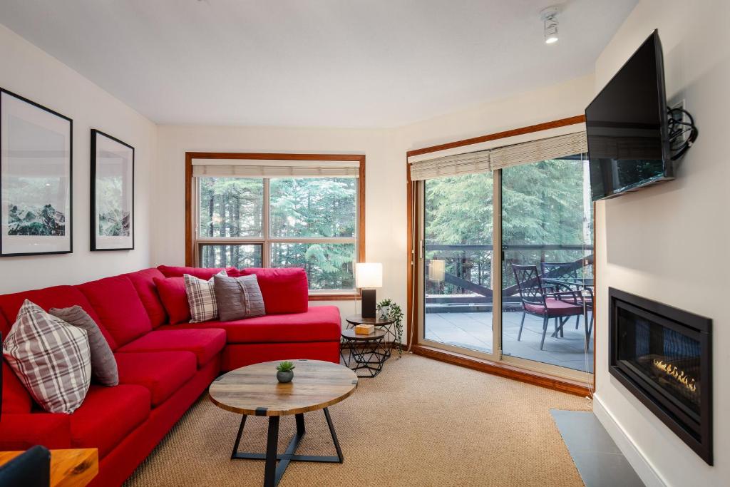 a living room with a red couch and a fireplace at Ski In Ski Out Apartment with Pool and Hot Tub by Harmony Whistler in Whistler