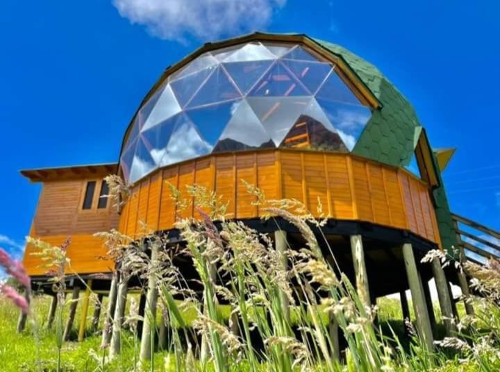 a building with a large window on top of a field at Colombia Mountain Tours Glamping and Cabanas in Choachí