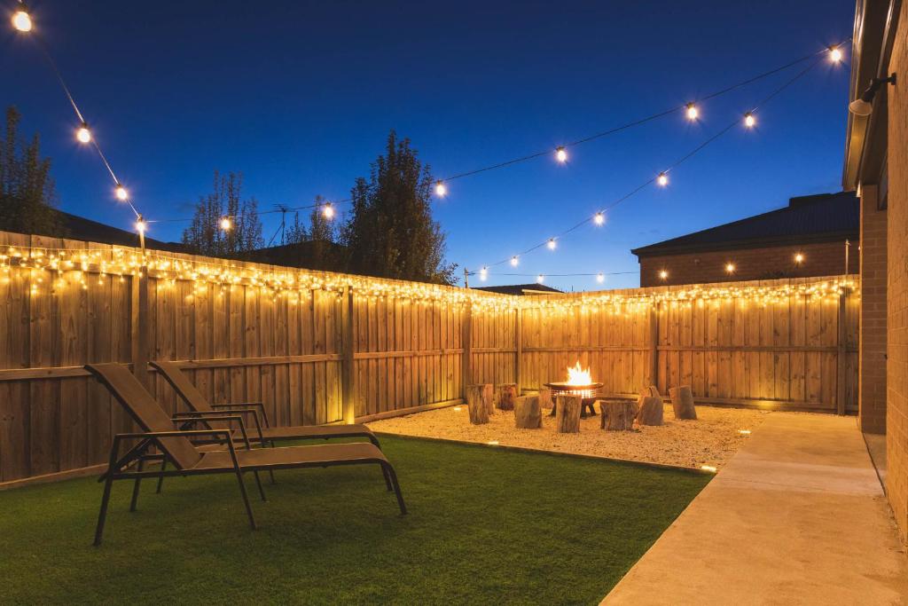 a backyard with a fence with lights and a fire pit at Tranquility Base, 3x King Beds, Huge, Fun Family Home in Saint Leonards