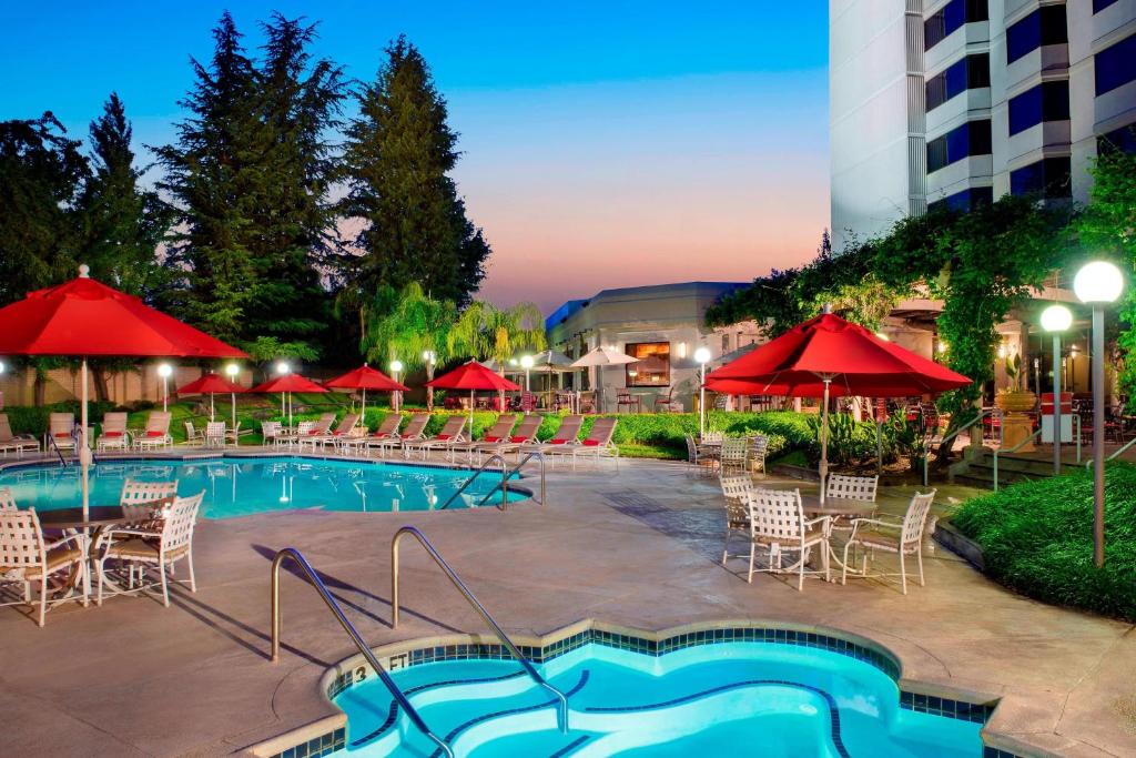 una piscina con sillas, mesas y sombrillas rojas en Sacramento Marriott Rancho Cordova, en Rancho Cordova