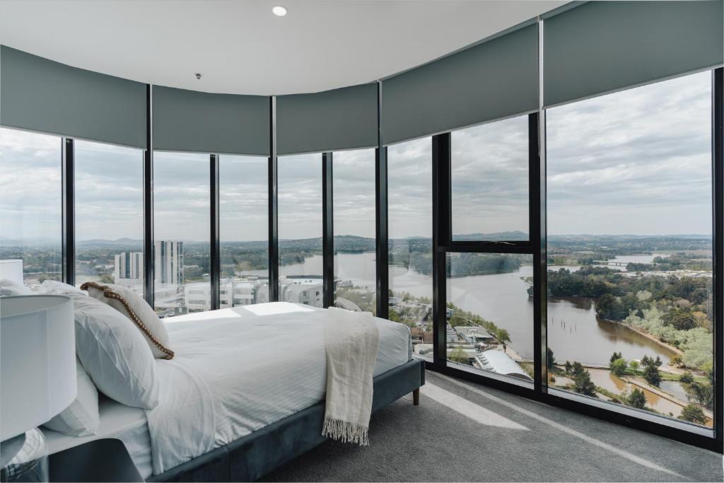 a bedroom with a bed and large glass windows at Panoramic Lake View 2-Bed with Pool, Gym and BBQ in Belconnen