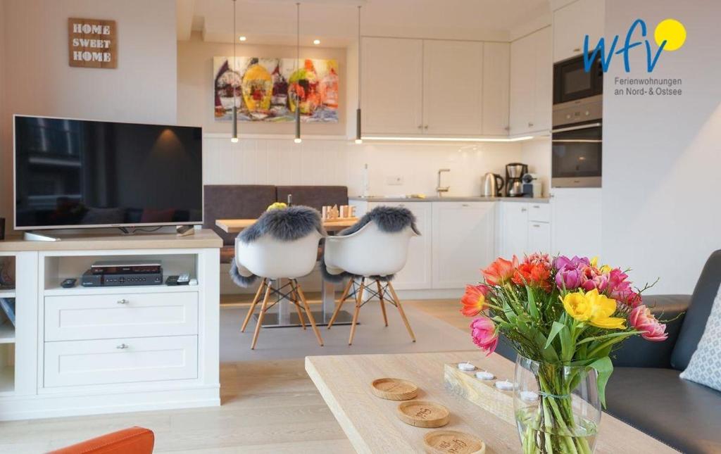 a living room with a television and a table with flowers at Achterhus - Ferienwohnung Wattwurm in Juist