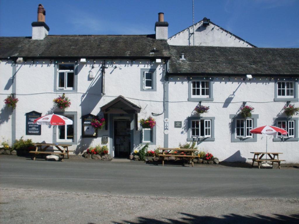 un bâtiment blanc avec des tables et des parasols devant lui dans l'établissement The Bridge Inn, à Holmrook