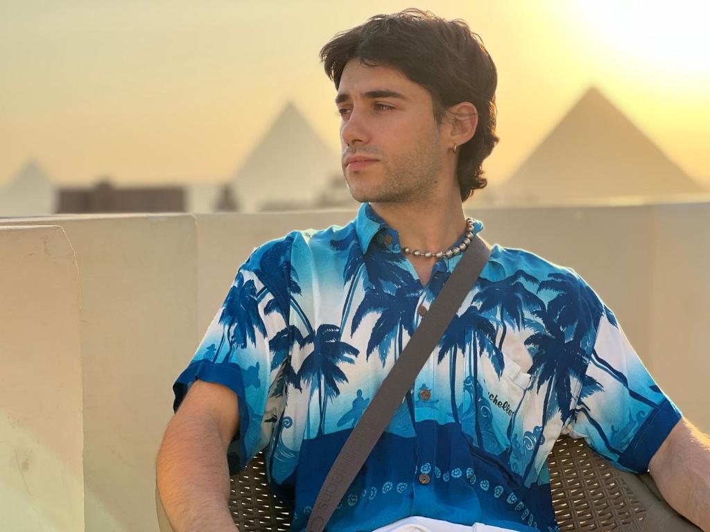 a man sitting on a bench wearing a blue shirt with palm trees at Lux pyramids View Inn in Cairo