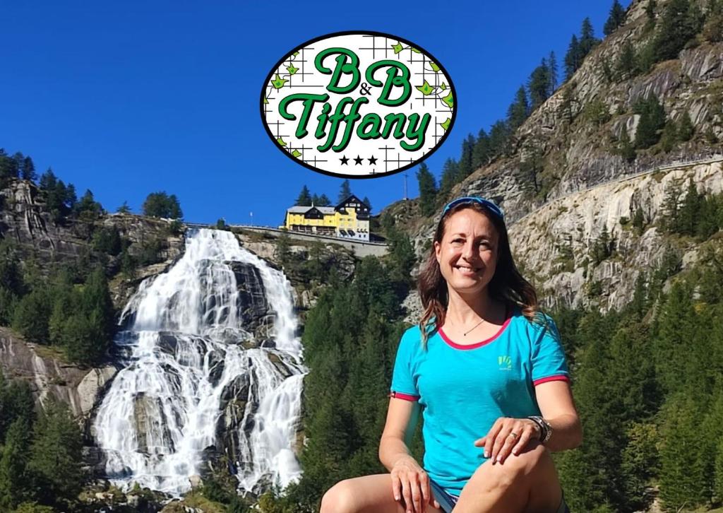 a woman sitting in front of a waterfall with a sign that says big thirsty at Bed & Breakfast Tiffany in Domodossola