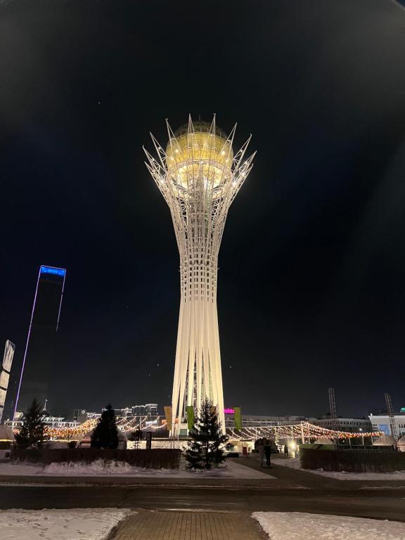 una torre alta con luces encendidas por la noche en 452 Возле Байтерека для компании 1-6 человек с 2 кроватями и диваном, en Astana