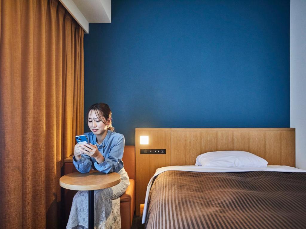 une femme assise dans une chambre d'hôtel en train de regarder son téléphone portable dans l'établissement Kansai Airport Washington Hotel, à Izumi-Sano