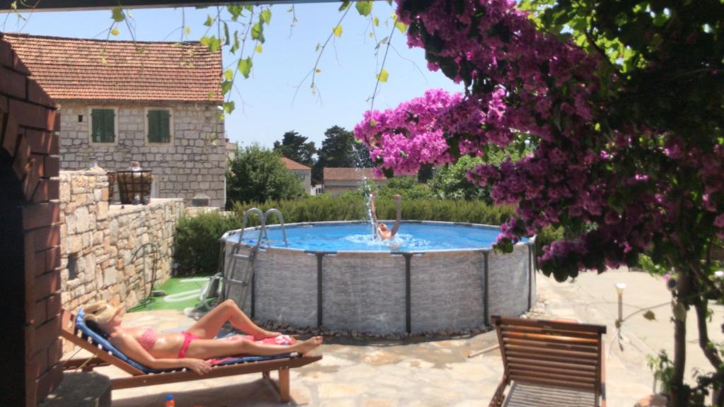 une femme assise sur une chaise de jardin devant une piscine dans l'établissement Holiday Home Bezic, à Grohote