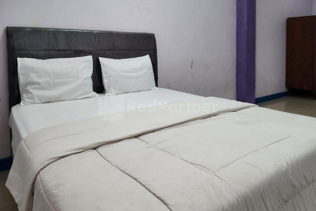 a large white bed with white sheets and pillows at Puspita Homestay Mitra RedDoorz in Jakarta