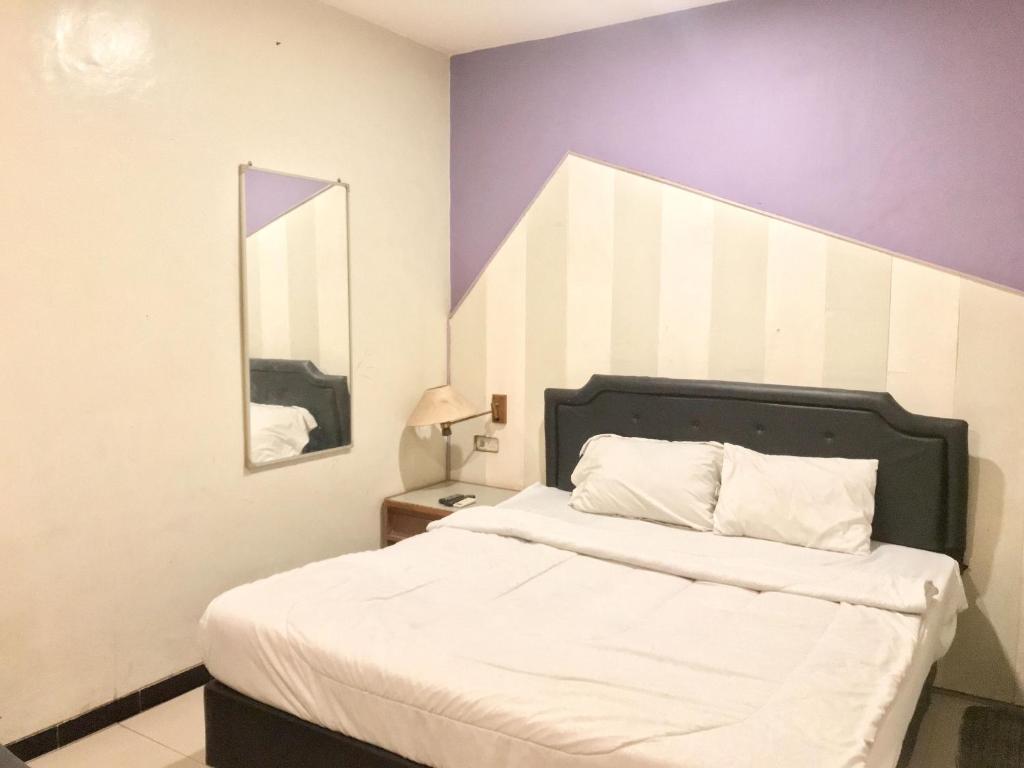 1 dormitorio con 1 cama blanca con espejo y paredes moradas en Gangnam Style Residence Mitra RedDoorz near MERR Surabaya, en Surabaya