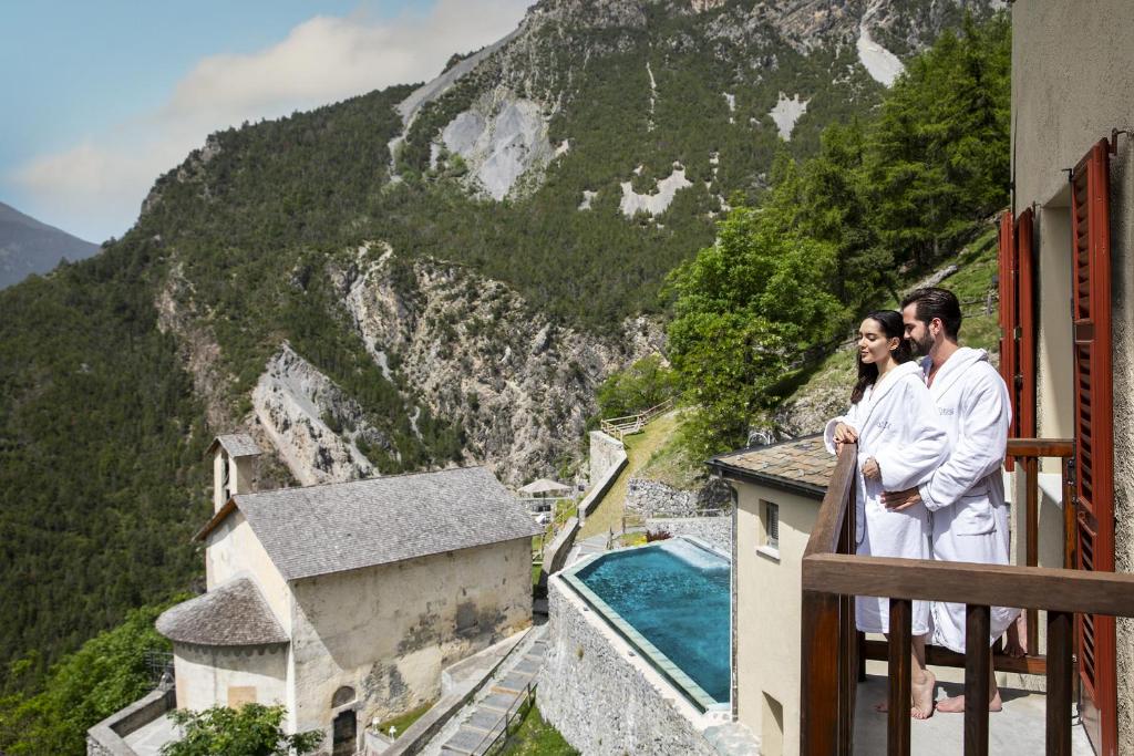 a man and woman standing on a balcony with a view of a mountain at QC Terme Hotel Bagni Vecchi in Bormio