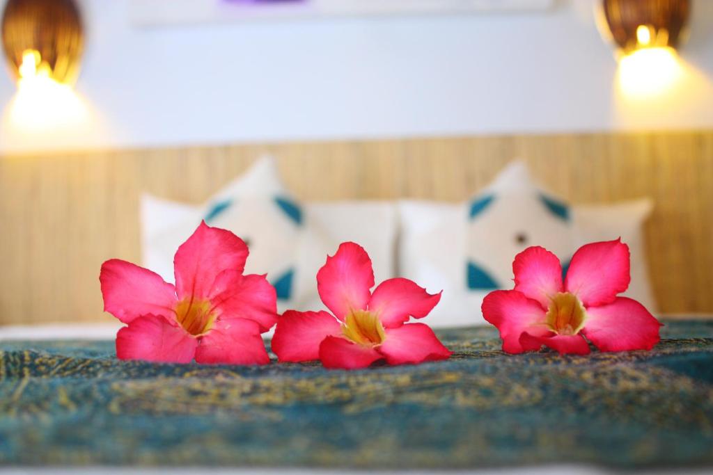 Kubu Betel Home Stay في تشانغو: ثلاثة زهور وردية على طاولة في غرفة