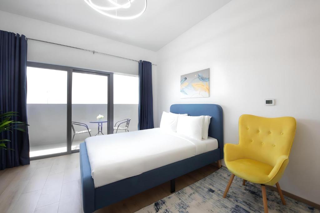1 dormitorio con 1 cama y 1 silla amarilla en Aura Azizi by Golden Casa, en Dubái