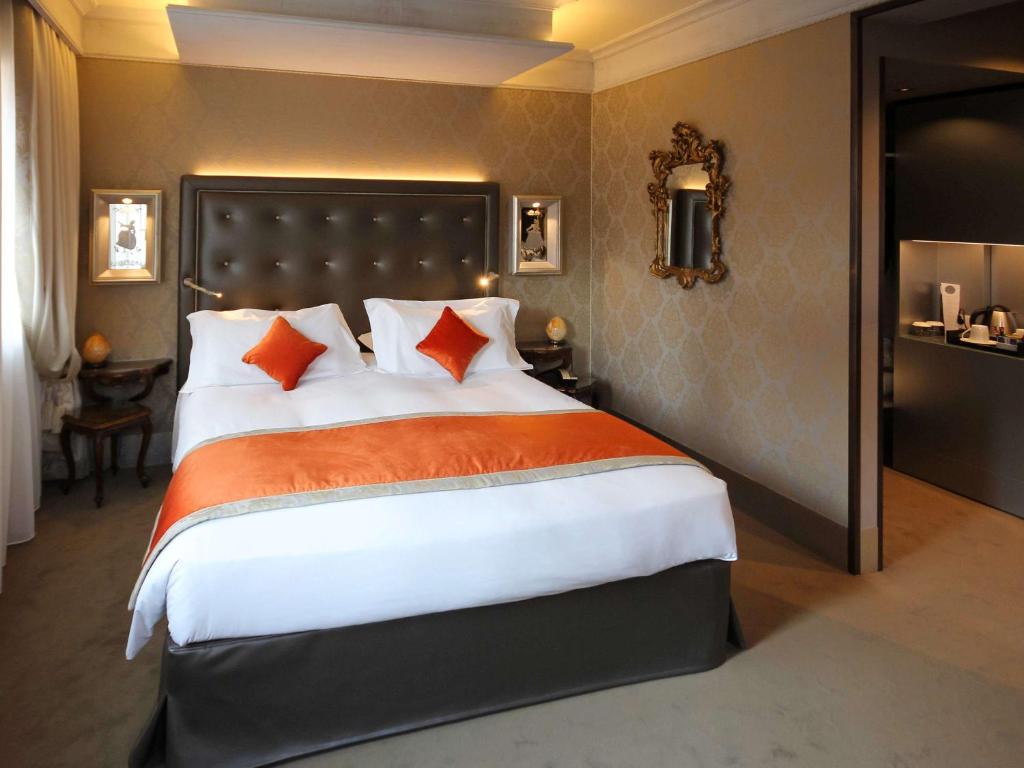 a bedroom with a large bed with orange and white pillows at Hotel Papadopoli Venezia - MGallery Collection in Venice