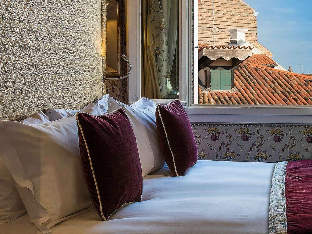 a bed with pillows sitting in front of a window at Hotel Papadopoli Venezia - MGallery Collection in Venice