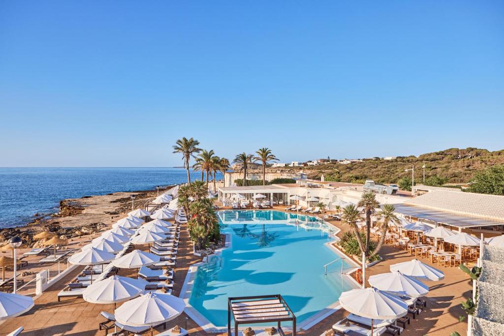 einen Pool mit Sonnenschirmen und Stühlen sowie das Meer in der Unterkunft AluaSoul Menorca - Adults Only in S'Algar