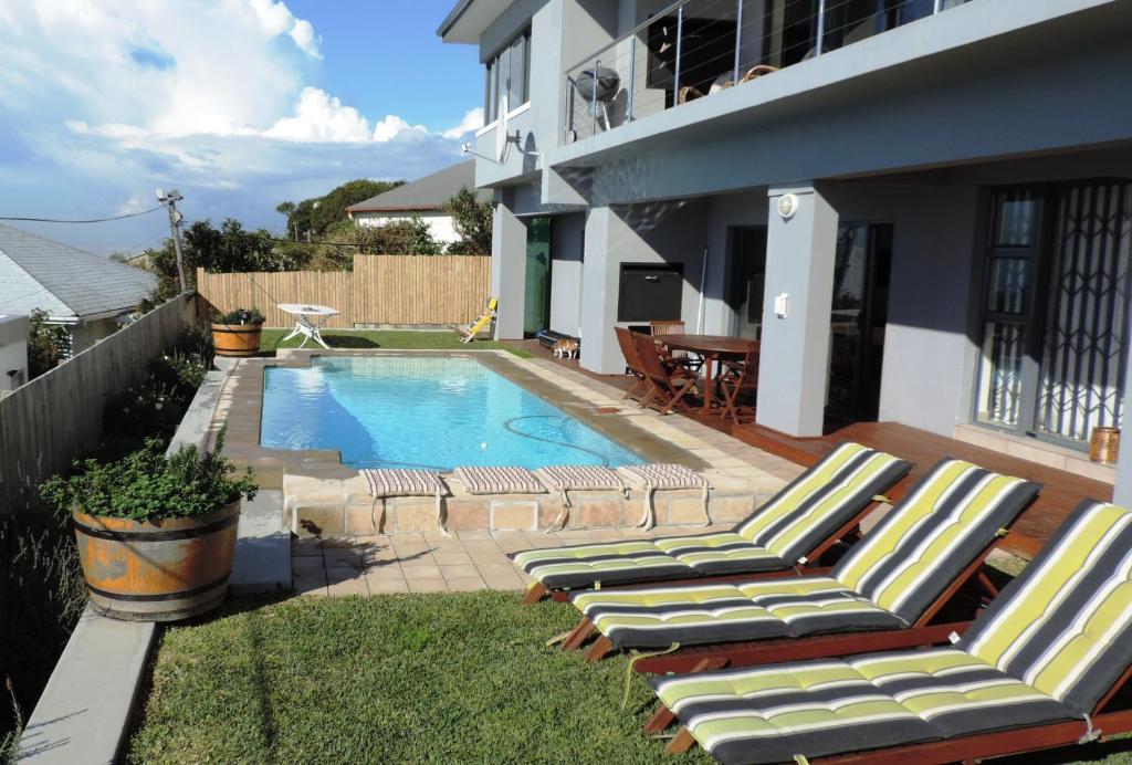 a swimming pool with lounge chairs next to a house at Blue Mountain Bay in Simonʼs Town