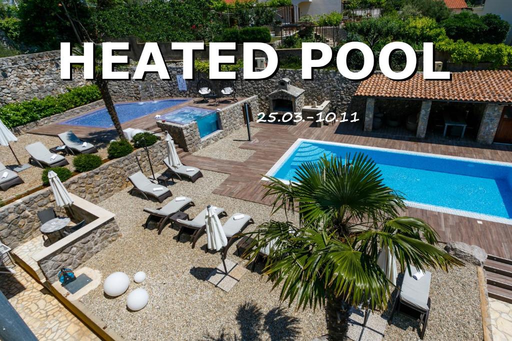 a heated pool with chairs and a palm tree next to it at Villa Palma Krk in Krk