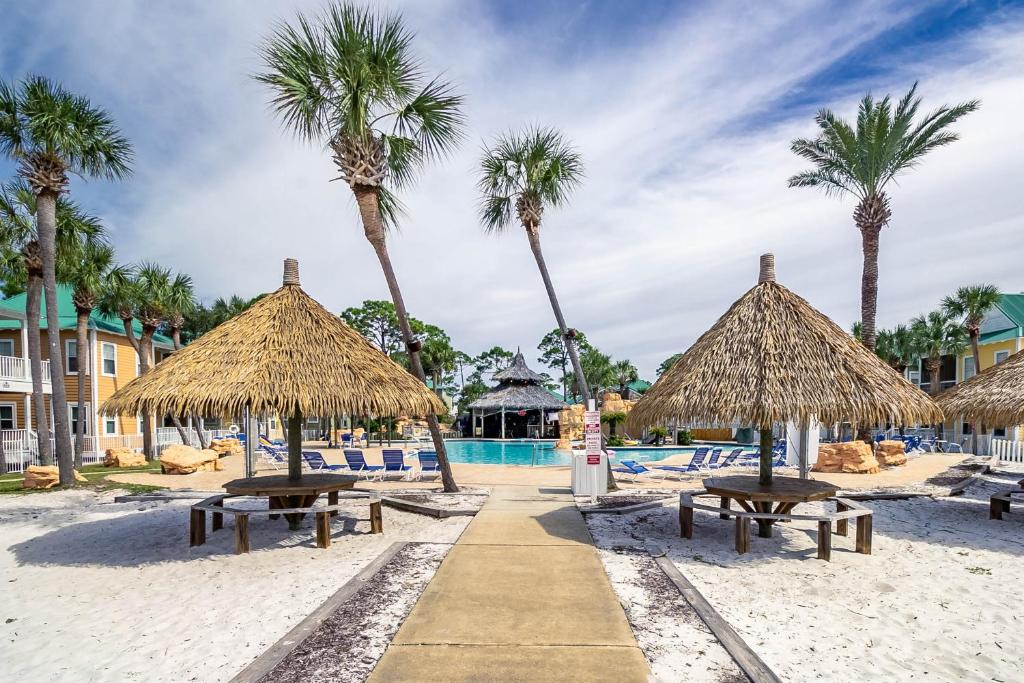 a beach with tables and straw umbrellas and palm trees at Five O'clock Somewhere 4Bd By Pkrm in Pensacola
