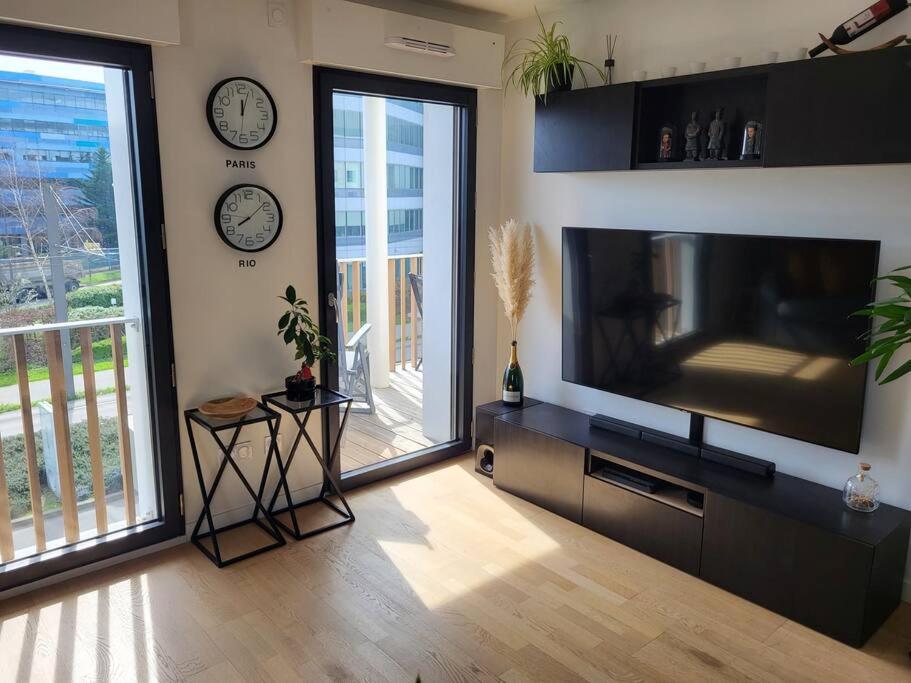 ein Wohnzimmer mit einem großen TV und einem Balkon in der Unterkunft Appartement Vélizy-Villacoublay in Vélizy-Villacoublay